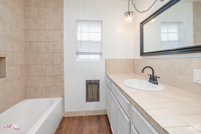 bathroom featuring a notable chandelier, backsplash, wood-type flooring, a bathtub, and vanity