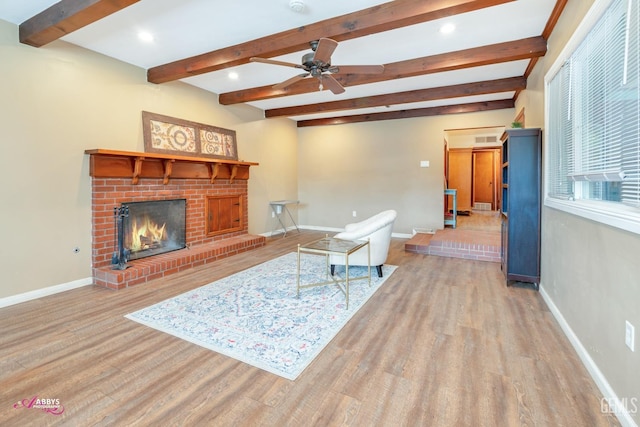 living room with beamed ceiling, ceiling fan, a fireplace, and light hardwood / wood-style flooring