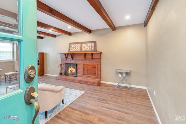 living room featuring hardwood / wood-style floors, beamed ceiling, and a brick fireplace