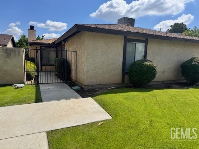 view of side of property with a gate, stucco siding, a yard, and a chimney