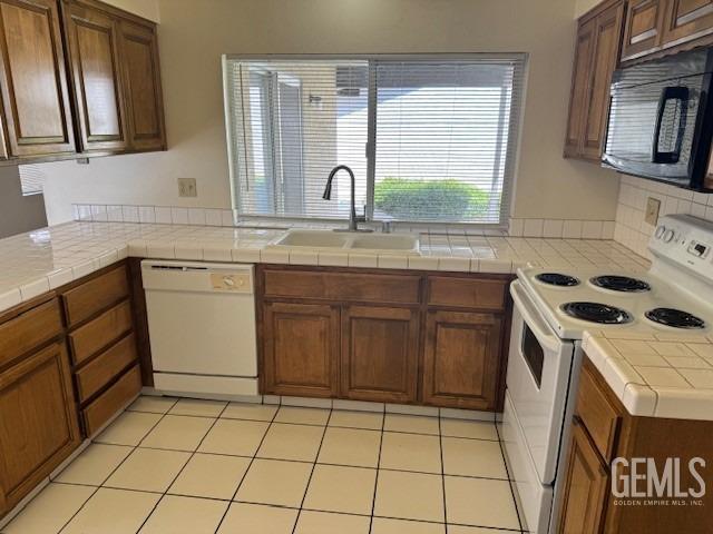 kitchen with a sink, tile counters, brown cabinetry, and white appliances