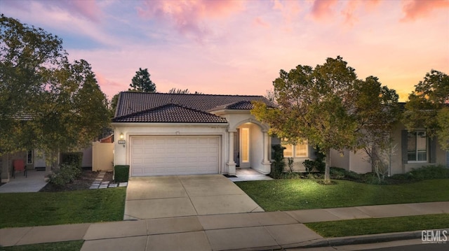 view of front of property featuring a front lawn, a tiled roof, stucco siding, a garage, and driveway