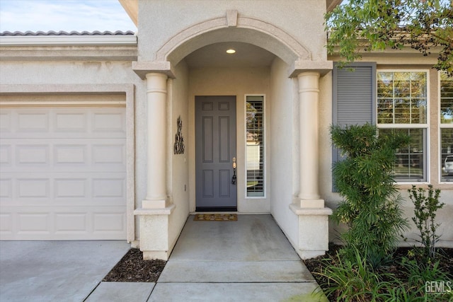 doorway to property featuring stucco siding, an attached garage, and concrete driveway