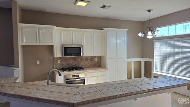 kitchen with an inviting chandelier, decorative light fixtures, appliances with stainless steel finishes, tile counters, and white cabinets