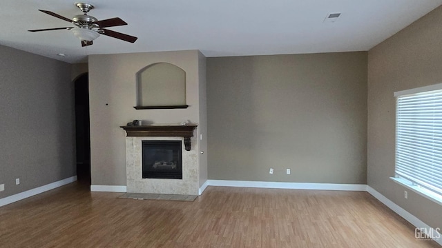 unfurnished living room with a tiled fireplace, light hardwood / wood-style floors, and ceiling fan