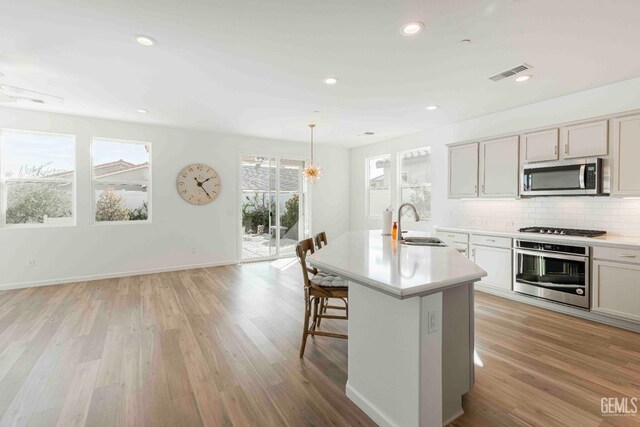 14209 Boon Way, Bakersfield, CA 93311 - kitchen with hanging light fixtures, a center island with sink, stainless steel appliances, light hardwood / wood-style floors, and decorative backsplash
