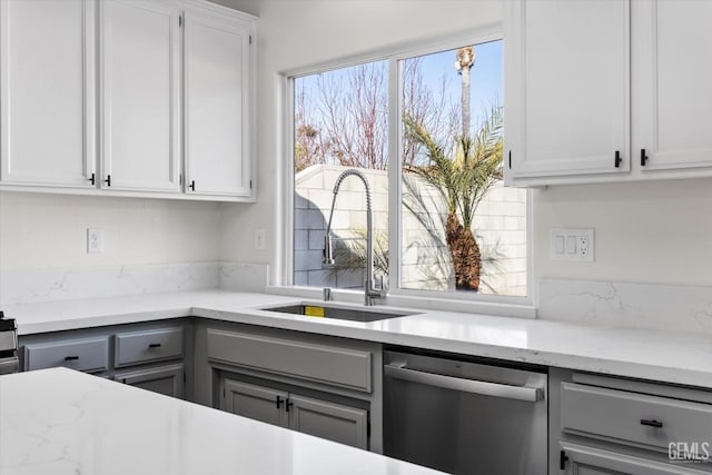 kitchen with white cabinetry, light stone countertops, sink, and stainless steel dishwasher