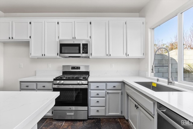 kitchen with white cabinetry, stainless steel appliances, light stone countertops, and sink