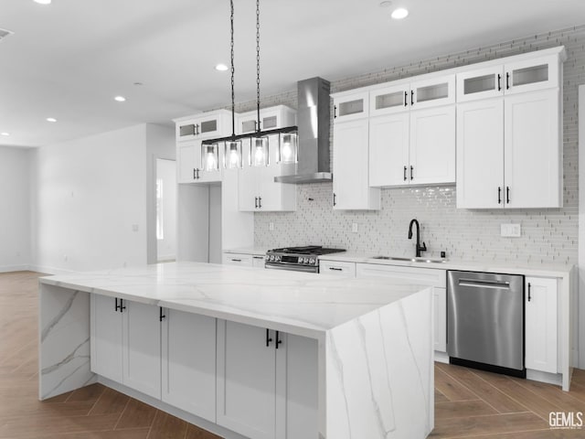 kitchen featuring white cabinetry, wall chimney exhaust hood, appliances with stainless steel finishes, and a sink