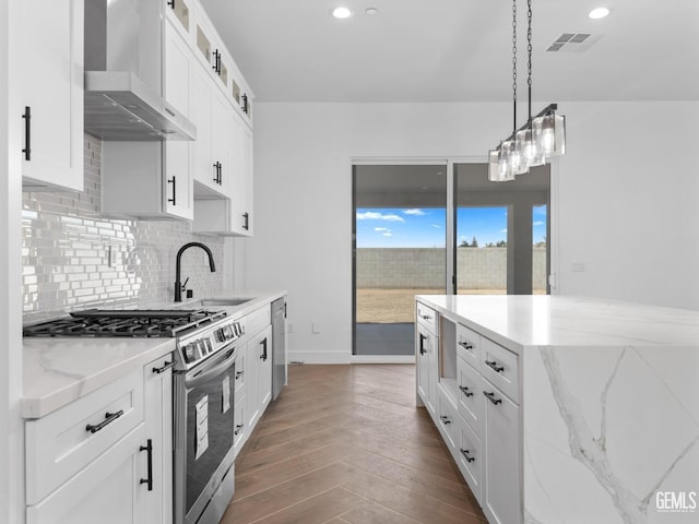 kitchen with a sink, visible vents, appliances with stainless steel finishes, backsplash, and wall chimney exhaust hood