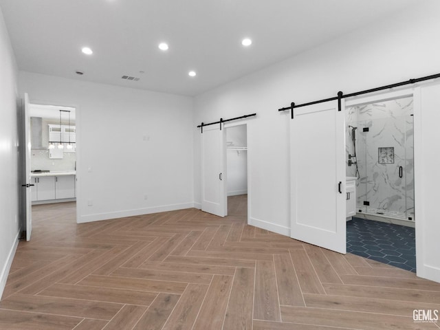 unfurnished bedroom featuring recessed lighting, a walk in closet, connected bathroom, and a barn door