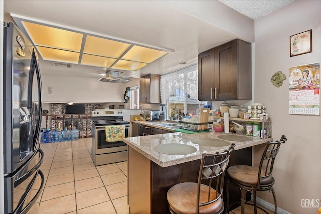 kitchen featuring a breakfast bar, kitchen peninsula, appliances with stainless steel finishes, light stone counters, and dark brown cabinetry