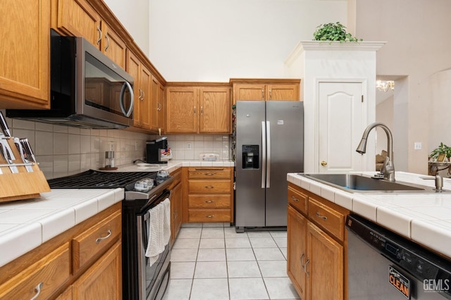 kitchen featuring light tile patterned floors, stainless steel appliances, tile counters, and sink