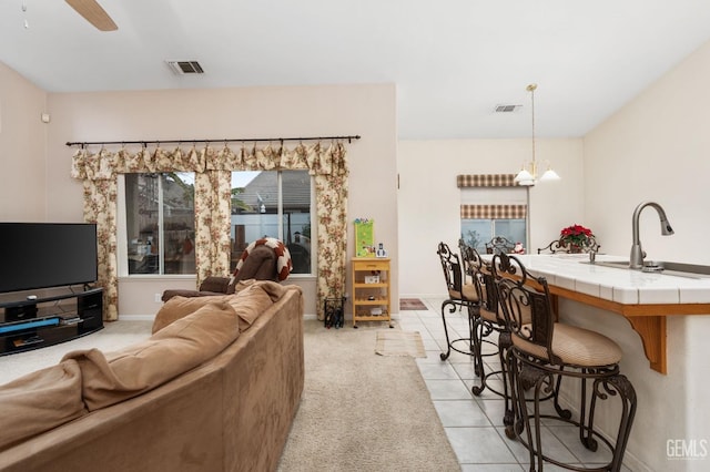 tiled living room featuring ceiling fan with notable chandelier and sink