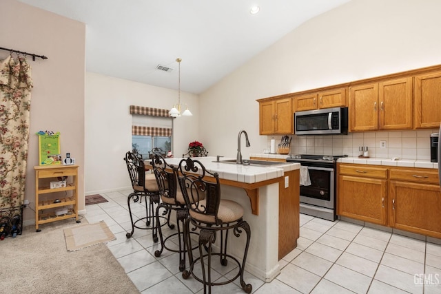 kitchen featuring appliances with stainless steel finishes, sink, a center island with sink, decorative light fixtures, and lofted ceiling