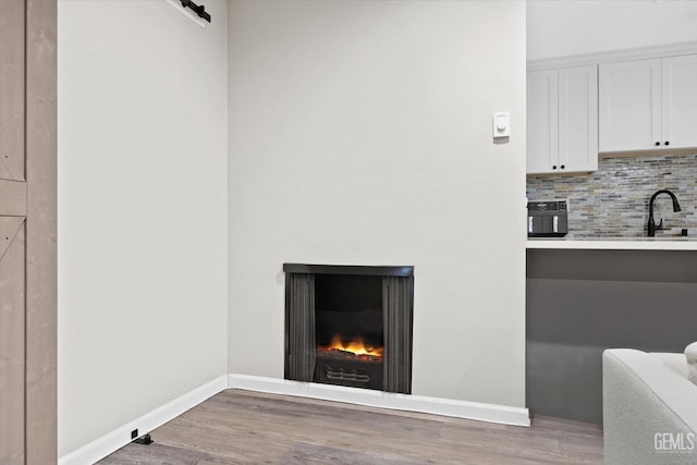 details featuring baseboards, a warm lit fireplace, white cabinets, decorative backsplash, and wood finished floors