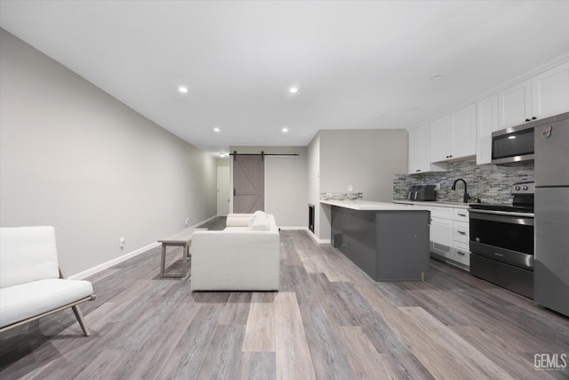 kitchen with tasteful backsplash, white cabinets, a barn door, light countertops, and stainless steel appliances