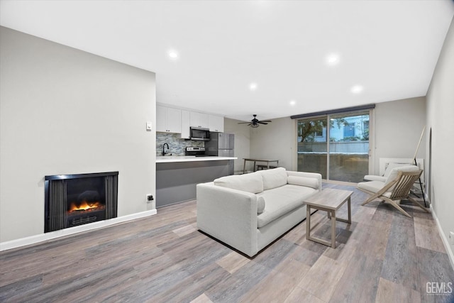 living area featuring light wood-type flooring, a ceiling fan, a warm lit fireplace, and recessed lighting
