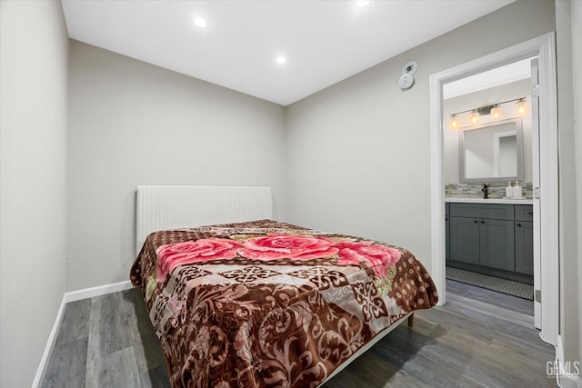 bedroom featuring ensuite bathroom, wet bar, wood finished floors, a sink, and baseboards