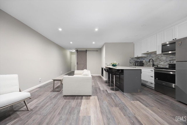 kitchen featuring stainless steel appliances, baseboards, white cabinetry, and a barn door