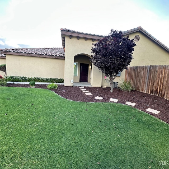 view of front facade with fence, a tiled roof, stucco siding, and a front lawn