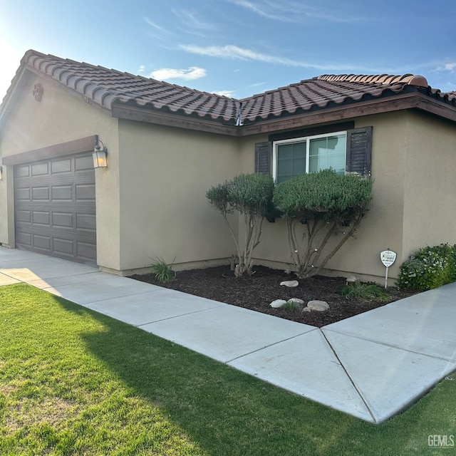 view of home's exterior with a garage, stucco siding, a lawn, a tiled roof, and driveway