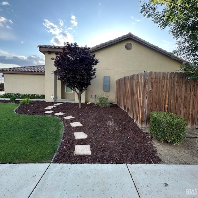 view of property exterior featuring stucco siding, fence, a yard, and a tile roof
