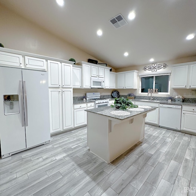 kitchen with visible vents, white appliances, a center island, white cabinetry, and vaulted ceiling