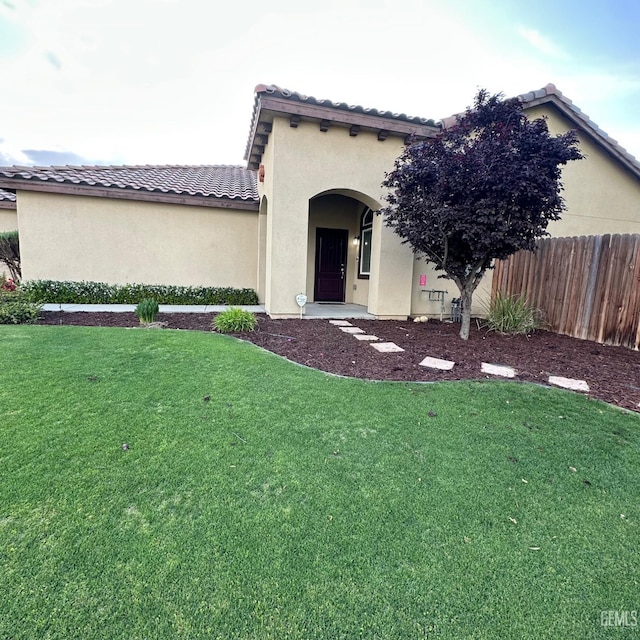 mediterranean / spanish home featuring fence, a tiled roof, stucco siding, and a front lawn