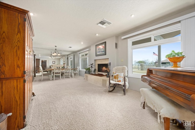 sitting room featuring visible vents, a tiled fireplace, an inviting chandelier, carpet flooring, and a textured ceiling