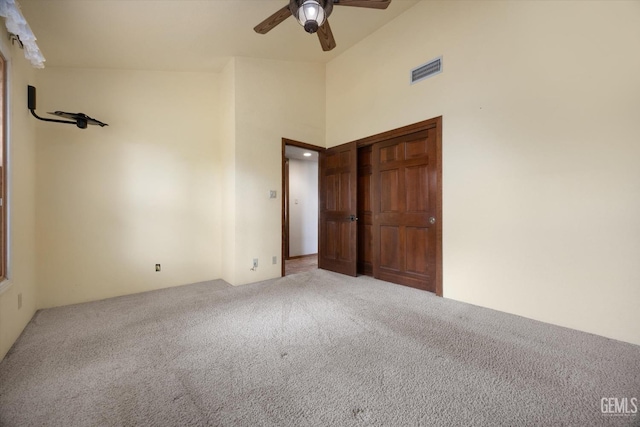 unfurnished bedroom featuring carpet, a towering ceiling, visible vents, and a ceiling fan