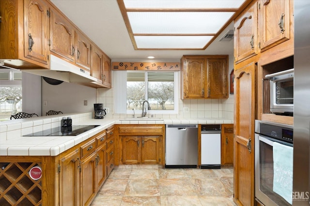 kitchen featuring a sink, visible vents, appliances with stainless steel finishes, decorative backsplash, and brown cabinets