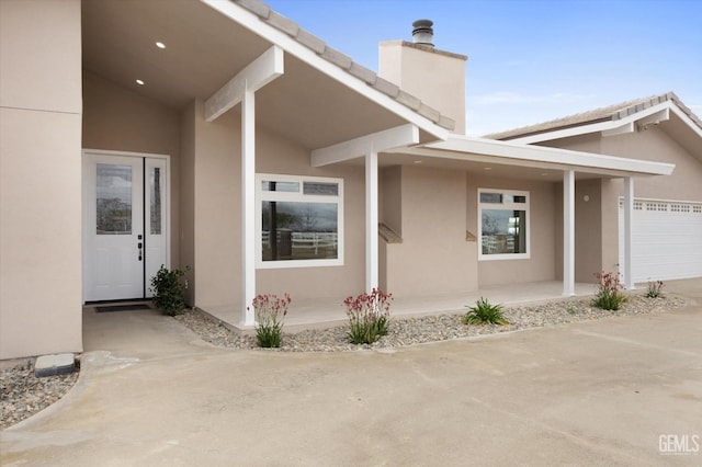 doorway to property featuring a garage, a chimney, a porch, and stucco siding