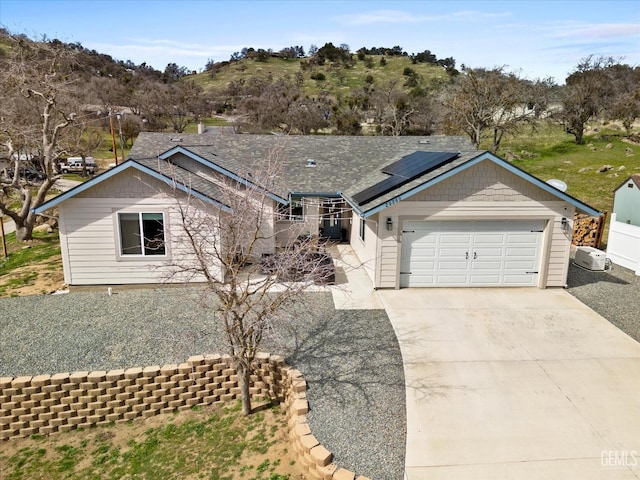 ranch-style house featuring driveway, a garage, and solar panels