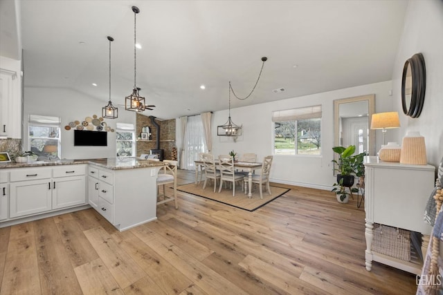 kitchen featuring a wood stove, light wood finished floors, a peninsula, and white cabinetry