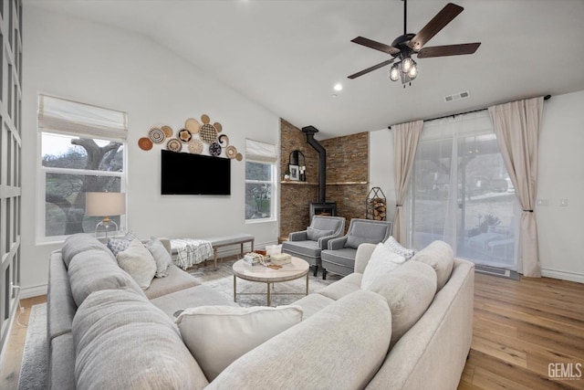 living room with visible vents, lofted ceiling, ceiling fan, wood finished floors, and a wood stove