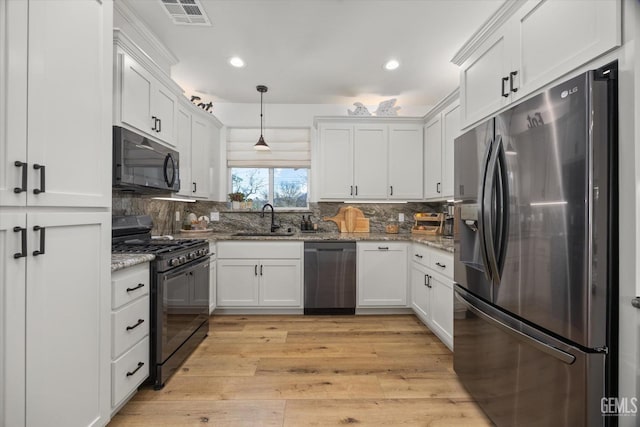 kitchen featuring light wood finished floors, visible vents, white cabinets, black appliances, and a sink