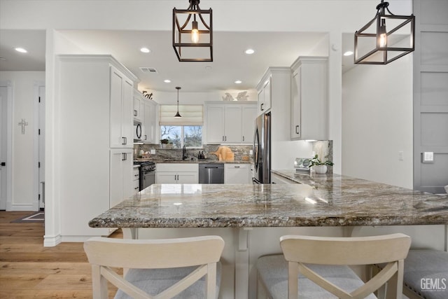 kitchen with light wood-style floors, a peninsula, stainless steel appliances, stone counters, and a sink