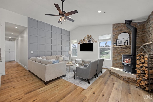 living room featuring baseboards, ceiling fan, a wood stove, vaulted ceiling, and light wood-style floors