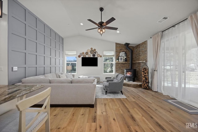 unfurnished living room with visible vents, ceiling fan, a wood stove, light wood-type flooring, and a decorative wall