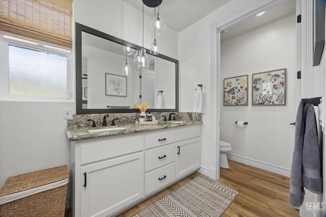 full bathroom with toilet, double vanity, a sink, and wood finished floors