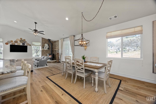 dining space with visible vents, a ceiling fan, lofted ceiling, a wood stove, and light wood-style floors