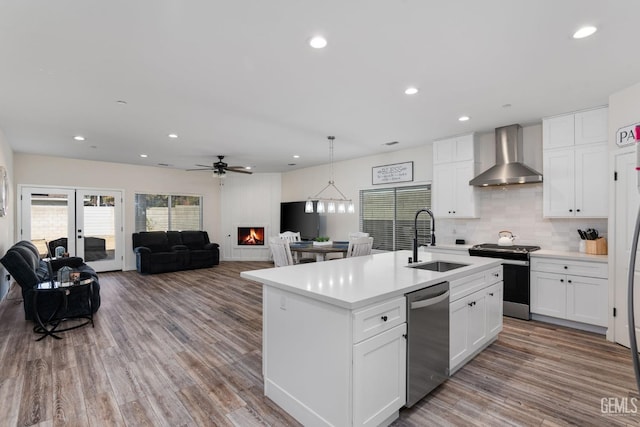 kitchen with wall chimney exhaust hood, white cabinetry, appliances with stainless steel finishes, and a kitchen island with sink