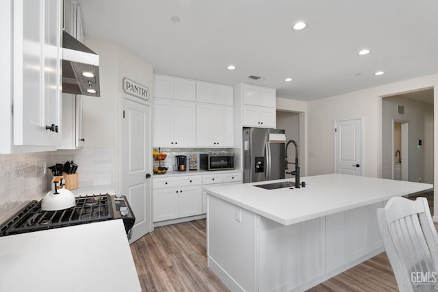 kitchen featuring appliances with stainless steel finishes, a kitchen island with sink, white cabinets, and light hardwood / wood-style flooring