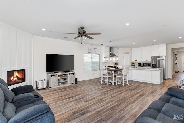 living room featuring ceiling fan, sink, a fireplace, and light hardwood / wood-style floors