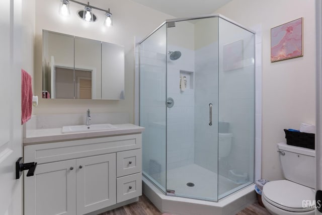 bathroom featuring vanity, hardwood / wood-style flooring, a shower with shower door, and toilet