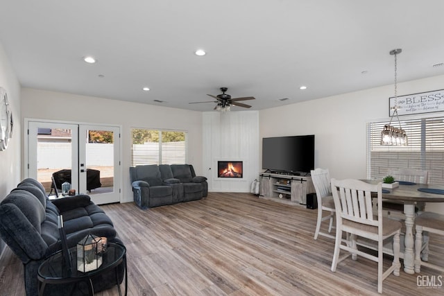 living room with ceiling fan with notable chandelier, a fireplace, light hardwood / wood-style floors, and french doors