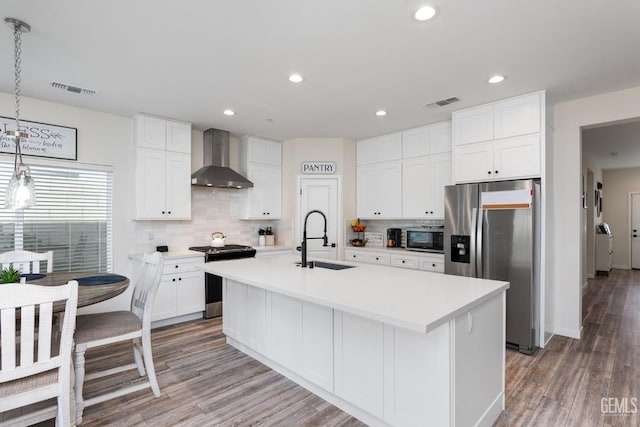 kitchen featuring appliances with stainless steel finishes, an island with sink, sink, white cabinets, and wall chimney exhaust hood