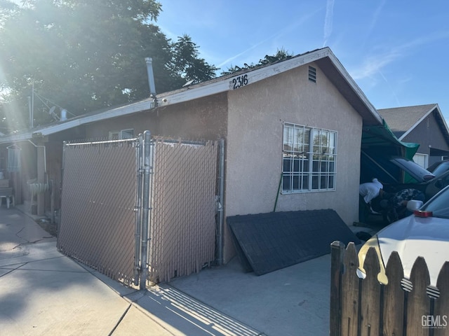 view of property exterior featuring stucco siding, fence, and a gate