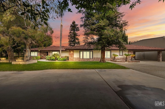 ranch-style house featuring stone siding, a front yard, a tiled roof, stucco siding, and a carport